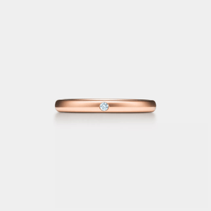 Rose gold ring with a small moissanite on a light gray background