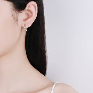 Silver earrings worn by a person with a plain background