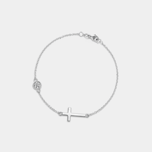 Gold bracelet with a small cross and round moissanite charm on a light gray background