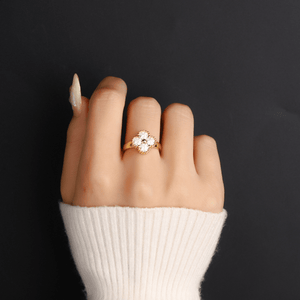 Hand wearing a gold ring with a floral design on a black background