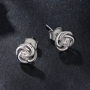 Silver knot earrings with clear gemstones on a dark fabric background