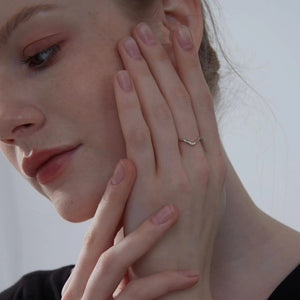 Close-up of a woman's face with one hand gently touching her cheek, wearing a gold ring.