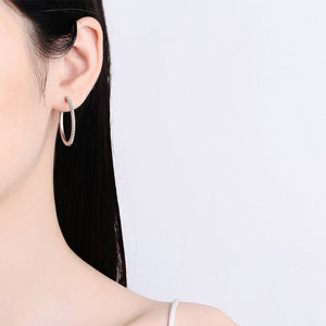 Close-up of an ear wearing a silver hoop earring on a plain background