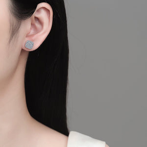 Close-up of a person wearing a silver earring with a clear gemstone on a neutral background