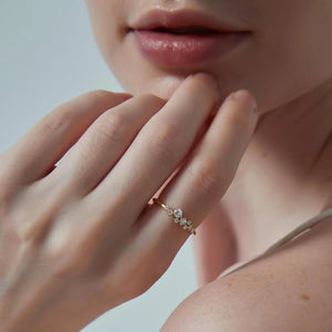 Close-up of a hand wearing a gold ring with diamonds, touching the chin against a neutral background.