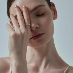 Woman with hand on face wearing a gold ring against a neutral background