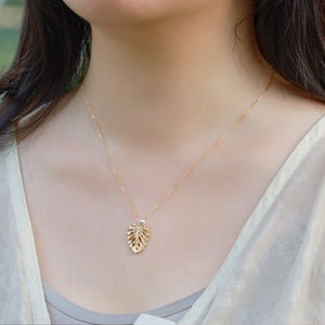 Gold necklace with a leaf pendant worn by a person