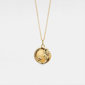 Gold necklace with a round locket featuring a moon face and star on a light gray background