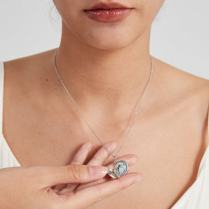 Sterling silver round locket necklace worn on a model, shown open to reveal a photo insert inside, held gently by hand.