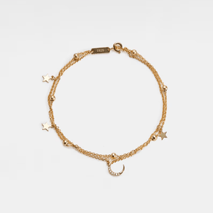 Gold bracelet with star and moon charms on a light gray background