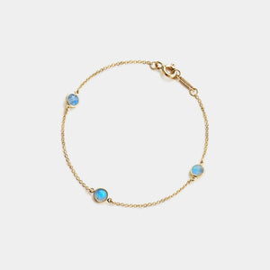 Gold bracelet with three blue gemstones on a light gray background
