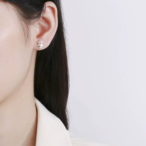Close-up of an ear wearing a silver earring with a clear gemstone on a plain background