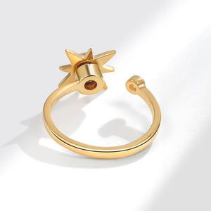 Gold spinner ring with star design and gemstone on a light gray background