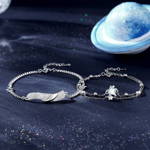 Two silver bracelets with star and feather designs on a dark blue fabric background.