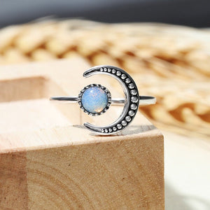 A silver-colored stacking ring with a crescent moon shape and a moonstone in the center, displayed on a white cushion.