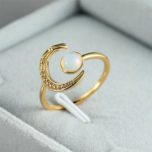 A gold-colored stacking ring with a crescent moon shape and a moonstone in the center, displayed on a soft fabric background