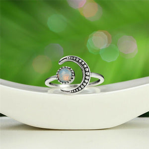 A silver-colored stacking ring with a crescent moon shape and a moonstone in the center, displayed on a white plate.