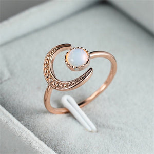 A gold-colored stacking ring with a crescent moon shape and a moonstone in the center, displayed on a soft fabric background