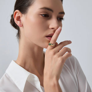 Woman wearing a gold ring with a green gemstone on a neutral background