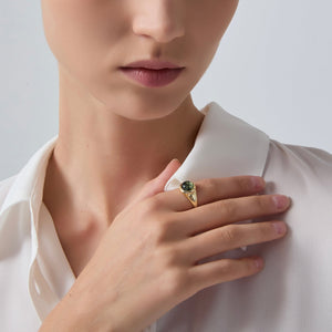 Close-up of a person wearing a gold ring with a green gemstone on a plain background