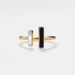 Gold ring with two rectangular stones, one black and one white, on a light gray background