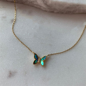 A gold-plated necklace with two butterfly pendants made of mother of pearl, displayed on a marble surface.