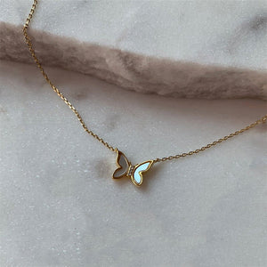 A gold-plated necklace with two butterfly pendants made of mother of pearl, displayed on a marble surface.