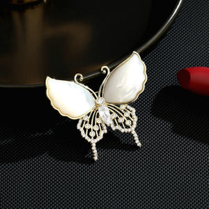A gold-plated butterfly brooch with white mother of pearl wings and embellishments made from cubic zirconia.