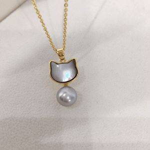 Cat-shaped pendant with a pearl on a gold chain against a white background