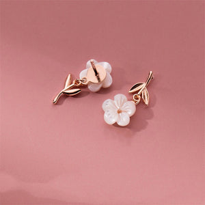 A set of sterling silver earrings with mother of pearl inlays designed to resemble cherry blossoms, displayed against a pink background.