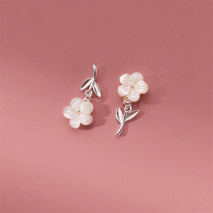 A set of sterling silver earrings with mother of pearl inlays designed to resemble cherry blossoms, displayed against a pink background.