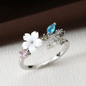 A collection of gold and silver floral bypass rings with mother of pearl and cubic zirconia accents displayed on a soft surface.