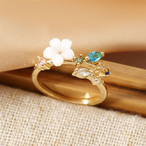 A collection of gold and silver floral bypass rings with mother of pearl and cubic zirconia accents displayed on a soft surface.