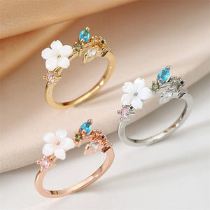 Three floral-themed rings in gold, rose gold, and silver on a beige fabric background.