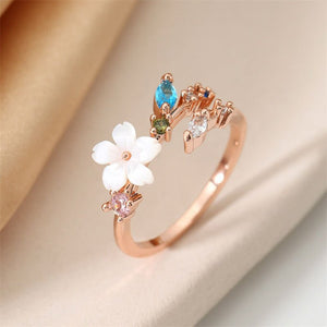 A collection of gold and silver floral bypass rings with mother of pearl and cubic zirconia accents displayed on a soft surface.