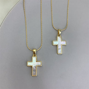 Two gold cross necklaces with white stone centers on a gray background
