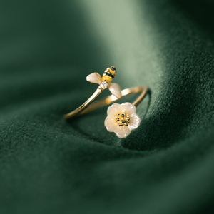 Delicate gold ring with a flower and bee design on a green fabric background