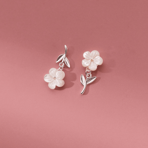 Floral earrings with pearl-like flowers and silver leaves on a pink background