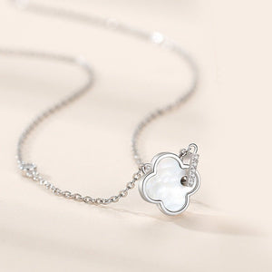 Silver necklace with a clover-shaped pendant on a light beige background