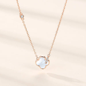 Rose gold necklace with a clover-shaped pendant on a beige background