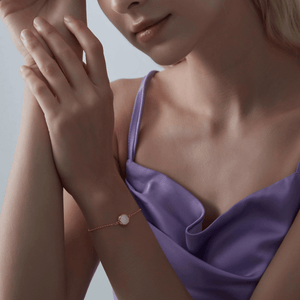 A woman wearing a gold bracelet featuring a small round mother of pearl locket with an adjustable chain.