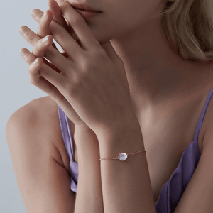 A woman wearing a gold bracelet featuring a small round mother of pearl locket with an adjustable chain.