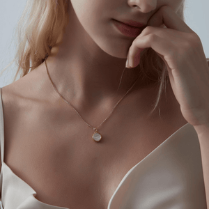 Woman wearing a rose gold necklace with a round mother of pearl locket on a light gray background