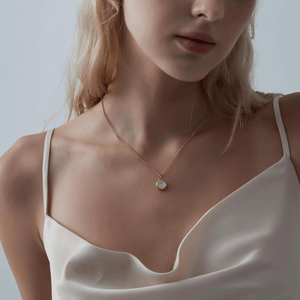 Woman wearing a rose gold necklace with a round mother of pearl locket on a light gray background
