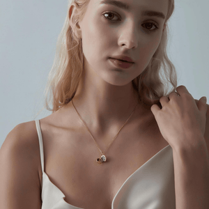 Woman wearing a rose gold necklace with a round mother of pearl locket on a light gray background