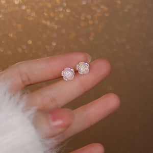 Hand holding pink rose-shaped earrings against a blurred background
