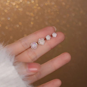 Hand holding three small rose-shaped earrings against a blurred gold background