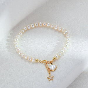 Pearl bracelet with gold starfish and shell charm on a light beige background