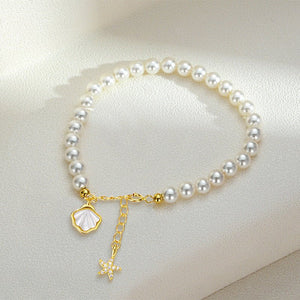 Pearl bracelet with gold starfish and shell charm on a light beige background