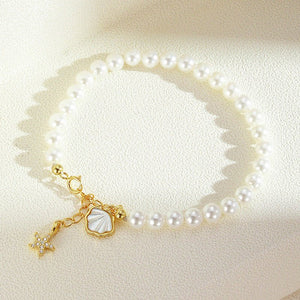 Pearl bracelet with gold starfish and shell charm on a light beige background